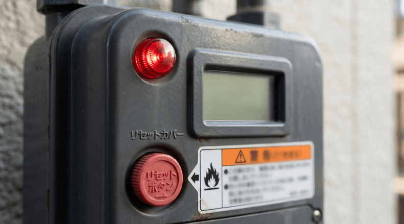  屋外に設置された家庭用ガスメーター、赤いランプが点滅している状態を示す